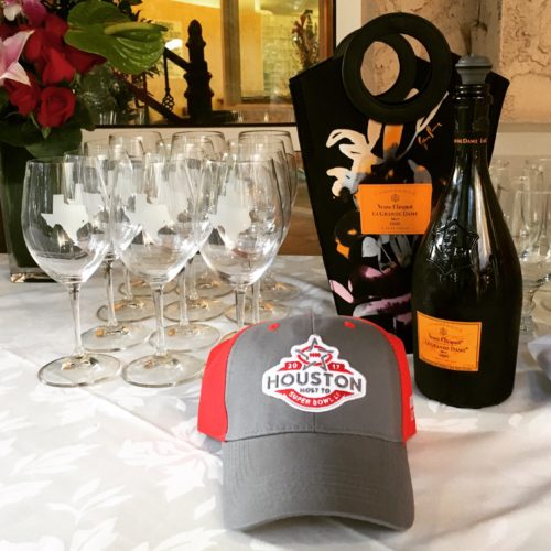 Wine glasses and a bottle of whine behind a hat with the Super Bowl LI logo on it