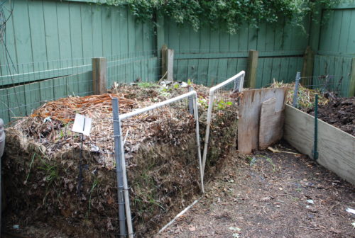 Composting area hidden behind decorative fencing and garden.