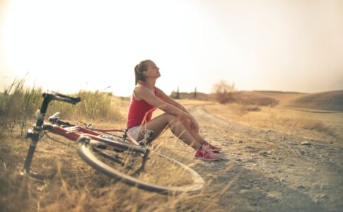 a happy woman sitting on the ground by a bike, finding a path to inner healing